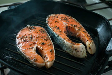 Two raw salmon steaks with spices and herbs on a grill pan. Close up bbq grilled salmon steaks on black cast-iron ribbed frying pan. Healthy, fitness food, diet. Selective focus