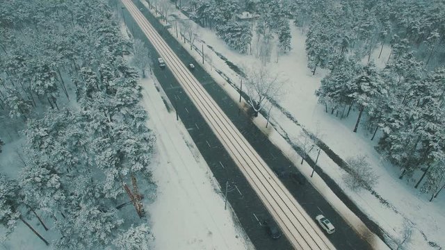 Above top view on winter forest road with cars and tram. Snowfall aerial drone footage