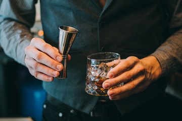 Bartender making alcoholic cocktail, metal jigger and bar environment