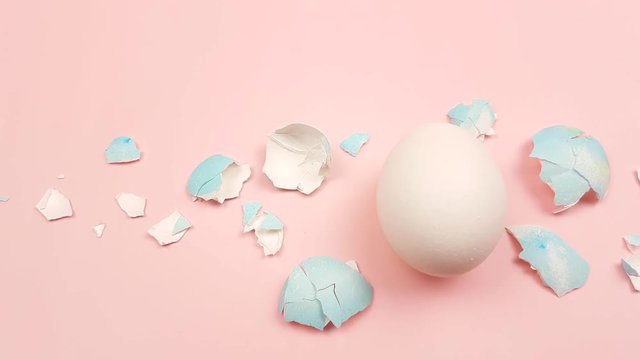 Eggshell with color easter egg on pastel pink background.