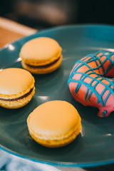 Tasty delicious yellow macaroons and donats on blue plate