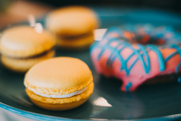 Tasty delicious yellow macaroons and donats on blue plate