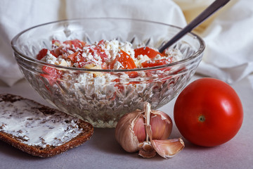 High protein diet salad - low fat cottage cheese, tomato, garlic and herbs in a vintage glass bowl, with a piece of wholegrain rye bread topped with soft cheese.