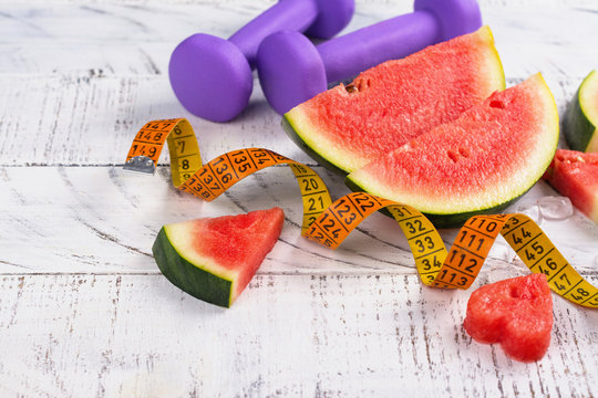 Fresh ripe watermelon slices, dumbbells and measuring tape on wooden background