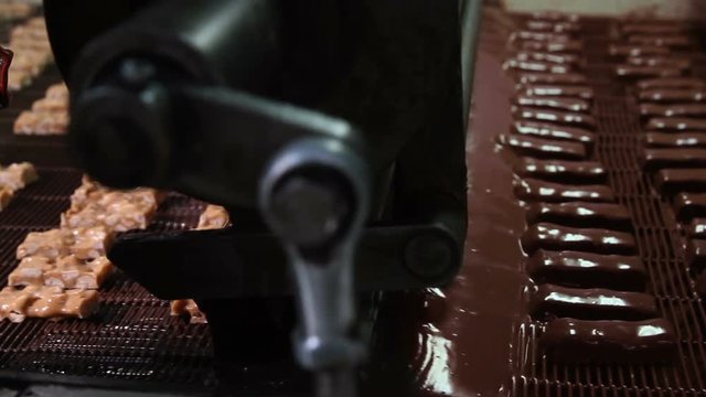 Bars of nougat with nuts are poured with chocolate. Manufacture of chocolate bars with nougat and peanuts. Chocolate bars move along conveyor belt at confectionery factory for the production of sweets
