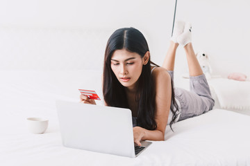 Woman shopping online with notebook and credit card on bed at home