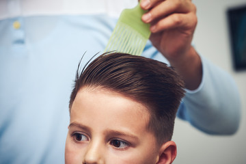 Fototapeta premium Barber is making a hairstyle to Caucasian boy in barbershop.