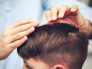 Naklejka premium Barber is making haircut to boy in barbershop. Close view.