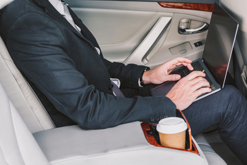 Handsome businessman working on laptop computer sitting on back seat of a car