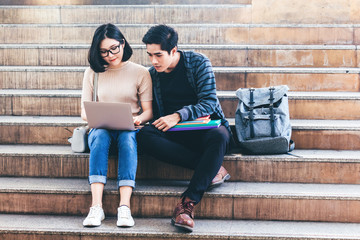 Two teenager students doing homework with books and laptop sit on stair at university