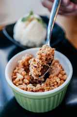 Apple crumble on a spoon with pastel color cup with ice cream vertical shot