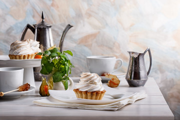 Delicious tartlets with meringue on top. Coffee and cupcakes served on white table.