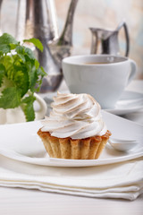 Delicious tartlets with meringue on top. Coffee and cupcakes served on white table.
