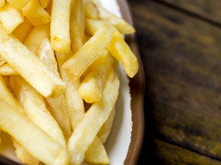 fried French fries on a white plate with brown border on the wooden table