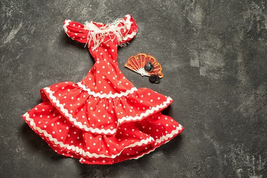 flamenco traditional dress for doll with fan and castanets on a black cement background, top view with copy space