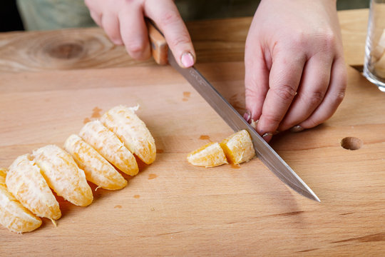 A woman cuts an orange with her knife on a wooden background. Close-up