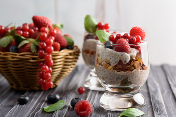 Two glasses of chia pudding with fresh strawberries, raspberries and blueberries. Basket with berries. On a wooden grey background.