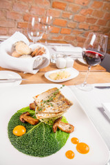 Fried zander, millet with green vegetables, fried boletus with thyme on a green leaf with some egg yolks served in a restaurant