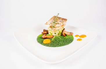 Fried zander, millet with green vegetables, fried boletus with thyme on a green leaf with some egg yolks on a white background