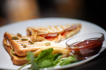 Sandwich with fish on a white plate with sauce and greens.