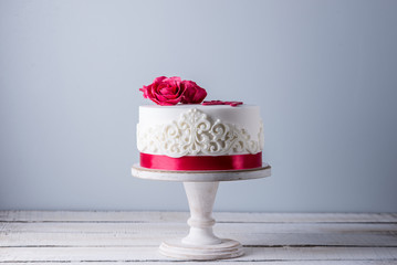 Beautiful white wedding cake decorated with flowers red roses and ribbon. Concept of elegant holiday desserts