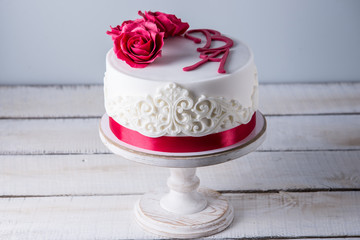 Beautiful white wedding cake decorated with flowers red roses and ribbon. Concept of elegant holiday desserts