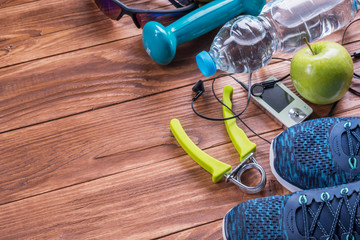 Set for sports activities on brown wooden background. Healthy lifestyle concept. Sport equipment, sport shoes, measuring tape, dumbbell, hand expander, apples and bottle of water