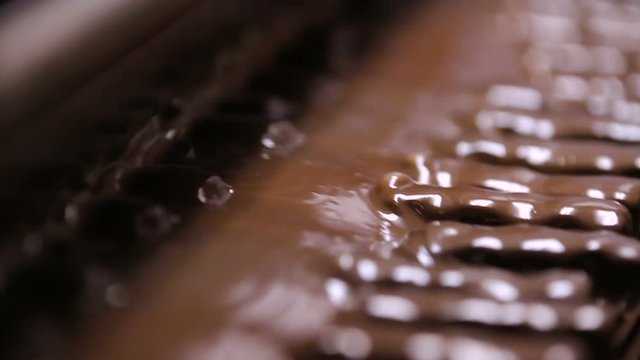 Bars of nougat with nuts are poured with chocolate. Manufacture of chocolate bars with nougat and peanuts. Chocolate bars move along conveyor belt at confectionery factory for the production of sweets