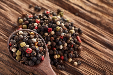 Top view of a wooden spoon full of allspice seeds isolated on wooden background, shallow depth of field, front focus