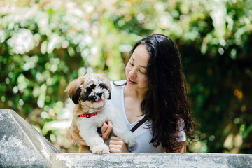 Image of a beautiful Asian woman carrying her dog Shih Tzuh. She wears a very casual white shirt and pants, and with her pet she seems to enjoy her day.