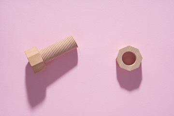 Hex nut and bolt on pink background. Build and repair concept, pop art. Wooden bolt and nut.