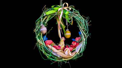 Easter wreath on a black background, braided from a vine, with colorful ribbons and hanging eggs