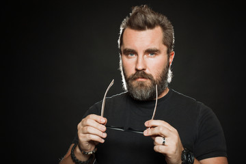 A handsome, strong man with a stylish hairstyle and beard dresses sunglasses in the Studio on a black background. With copy space for your text