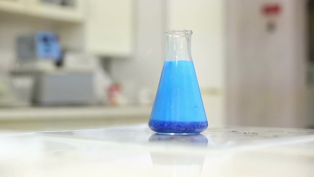 Cinemagraph of blue liquid boiling in glass conical flask standing on table in lab