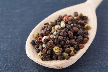 Top view of a wooden spoon full of allspice seeds isolated on dark background, shallow depth of field, front focus