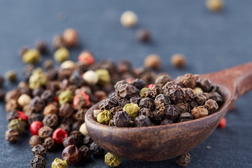 Top view of a wooden spoon full of allspice seeds isolated on dark background, shallow depth of field, front focus