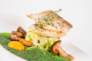 Fried zander, millet with green vegetables, fried boletus with thyme on a green leaf with some egg yolks on a white background