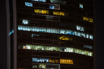 Close up view to office windows of skyscraper in downtown at night, working people within. Dubai, United Arab Emirates