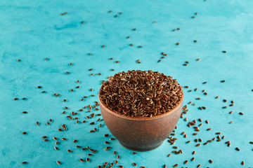 Flax seeds in a clay bowl isolated on blue background, close-up, selective focus, vertical.