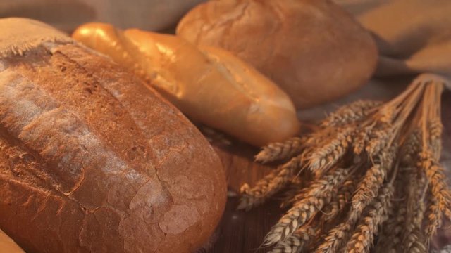 handmade tasty bread lying on burlap on the wooden table with flour, wheat and ears of wheat.