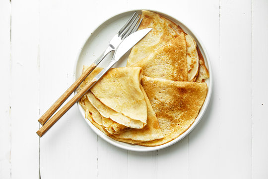 Overhead image of french crepes in white plate on wooden table