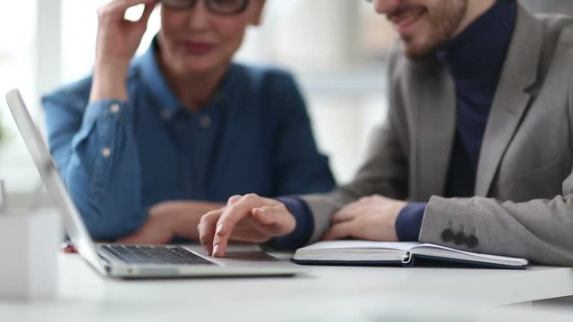 Cinemagraph of Caucasian man sitting in office with female colleague, using touchpad on laptop and smiling