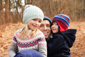 Obraz premium father hugging son and daughter outside at park during wintertime 