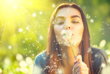 Beautiful young woman lying on green grass and blowing dandelions. Allergy free concept