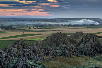 Beautiful rural landscape with old rocks, trees, fields smoke and a sunset sky,Dobrogea, Romania
