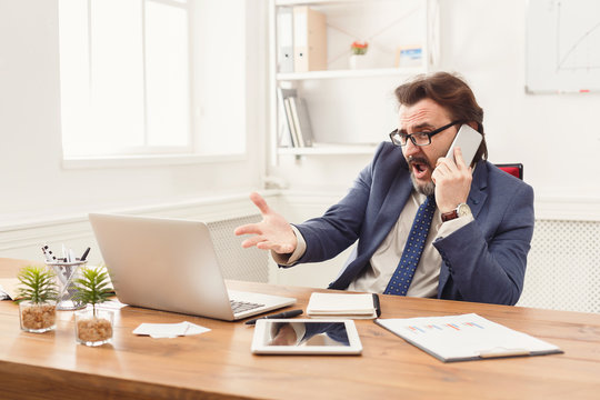Stressed businessman with laptop talking on phone