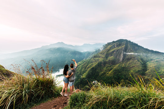 A couple in love is photographed on the phone. Boy and girl in the mountains. Man and woman holding hands. The couple travels around Asia. Travel to Sri Lanka. Serpentine in the mountains. Lover