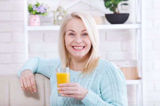 Woman drinking orange juice smiling. Beautiful middle aged Caucasian model face closeup.