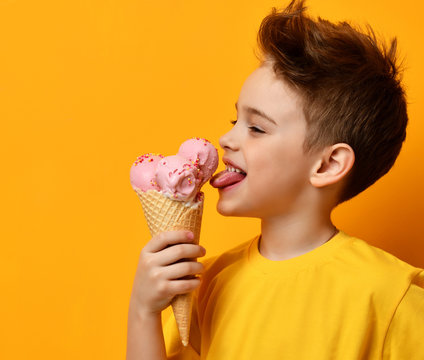 Baby boy kid eating licking strawberry ice cream in waffles cone on yellow 
