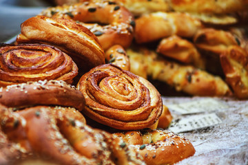 Fresh delicious cinnamon rolls placed on a table in outdoor market amongst other baked goods.